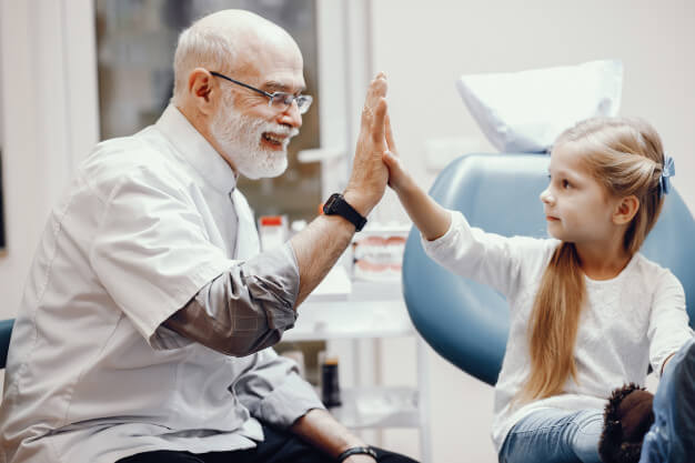 aposentadoria especial dentista profissional idoso sorrindo fazendo toque de mao com a paciente criança