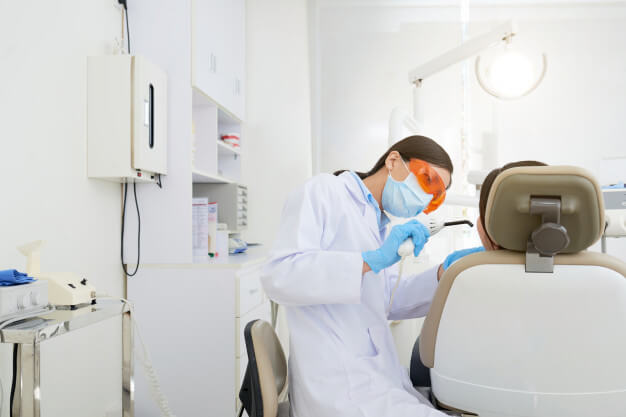 CRO dentista com oculos de proteção laranjado fazendo tratamento em paciente