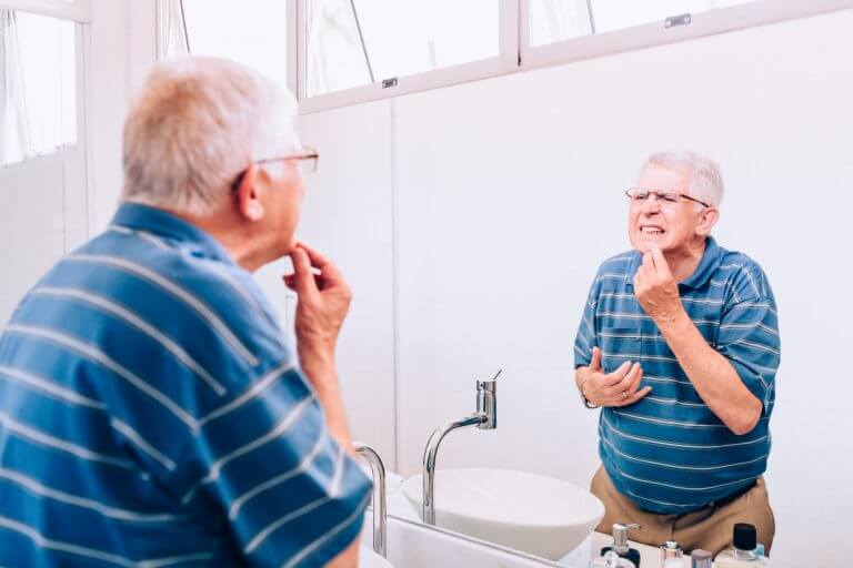 home care odontológico homem idoso olhando dentes no espelho