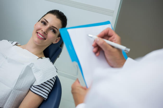 receita odontológica paciente sorrindo enquanto dentista escreve receita de medicamento